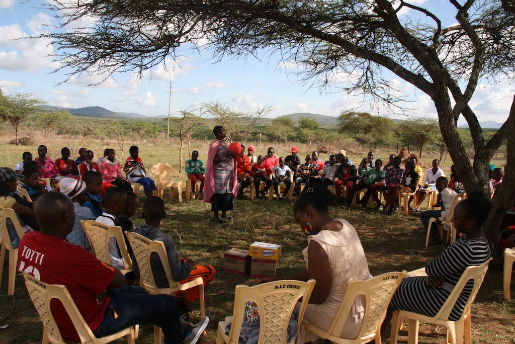 Community members sitting in a circle to hold an outdoor meeting under a tree. 