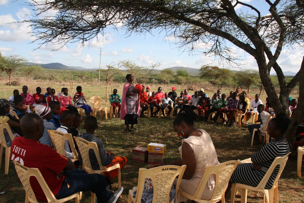Community members sitting in a circle to hold an outdoor meeting under a tree.
