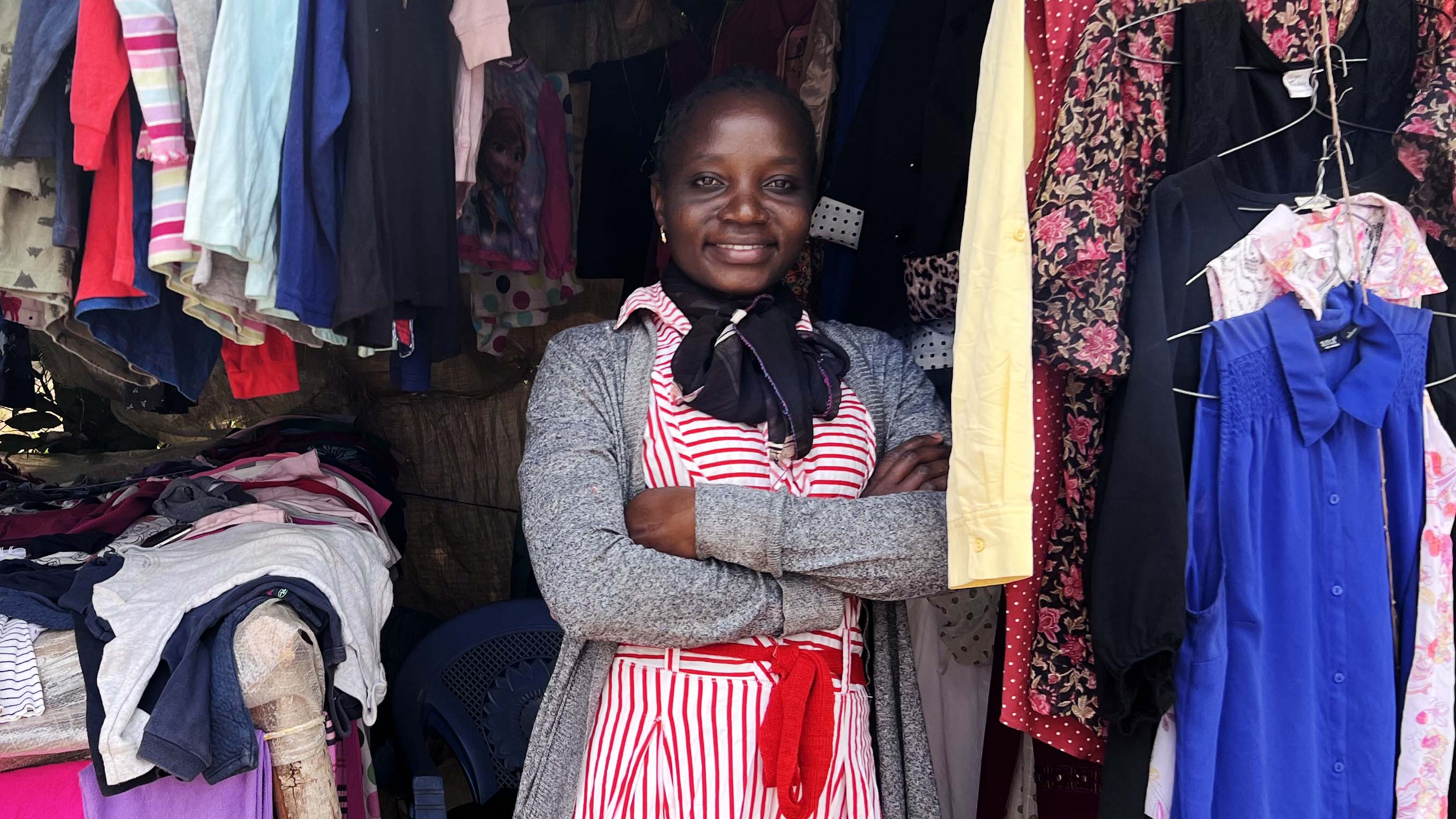 Female participant of entrepreneurship program run by Educate! standing in front of her clothing store.