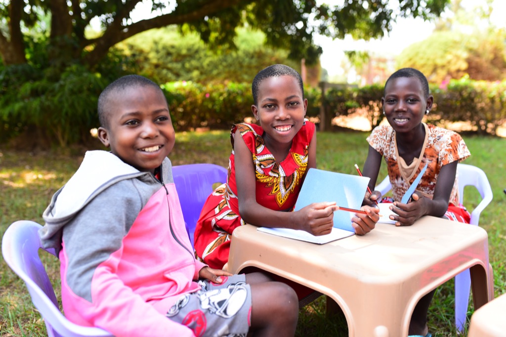 Three Kenyan girls sitting at a table smiling with notebooks and pencils.