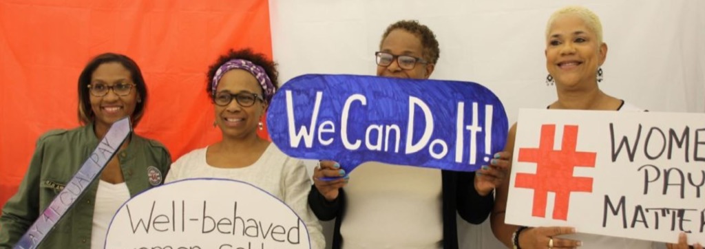 Three smiling women holding signs with women's empowerment messages that say: 1)"We Can Do it!" 2) "Equal pay" and 3) "Well-behaved women rarely make history.