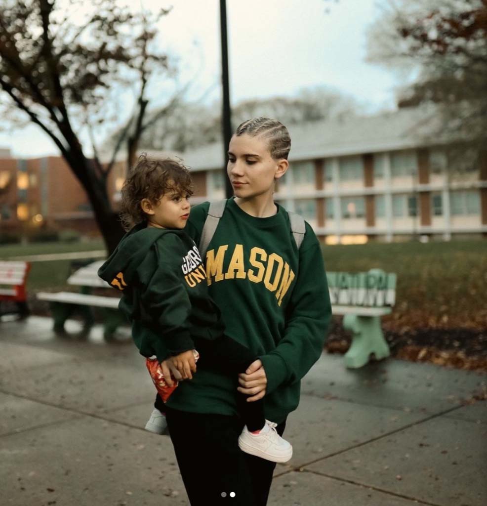 A student parent mom in a green sweater holding her son on campus.